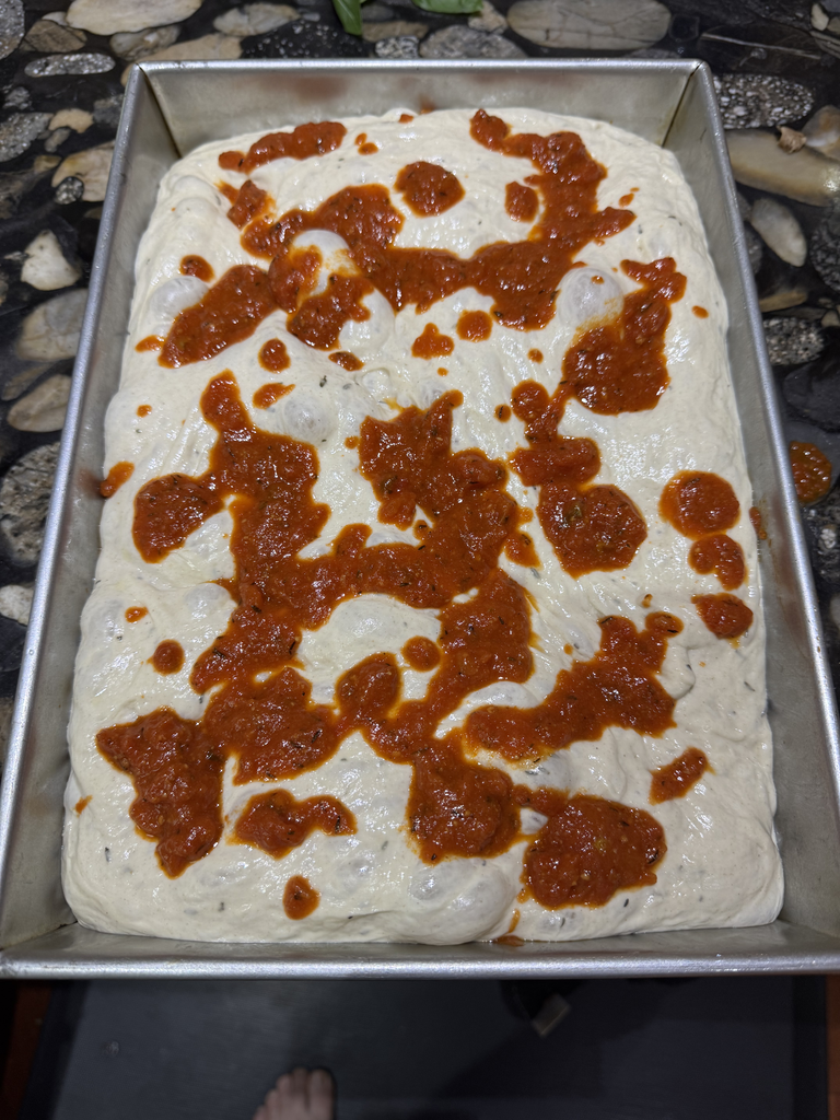 Pizza sauce gently dolloped over risen focaccia dough