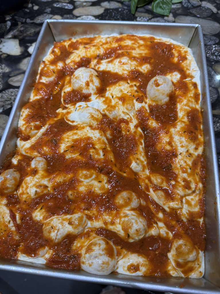 Sauce gently spread across dimpled focaccia pizza dough